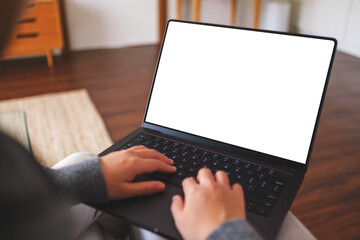 Mockup image of a woman working and typing on laptop computer with blank white desktop screen at...