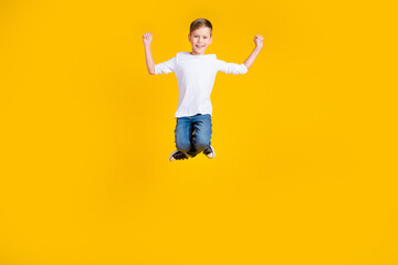 Obraz premium Full length photo of carefree lucky boy wear white shirt jumping high rising fists isolated yellow color background