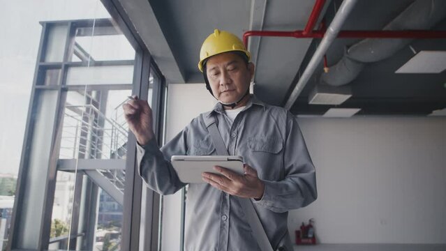 Low angle of adult Asian specialist in uniform and hardhat measuring window width and length inside building under construction
