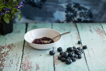 Blueberry pile next to blueberry jam in white bowl.