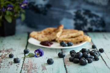 Pancakes on a white plate with a pile of blueberries and blueberry jam.