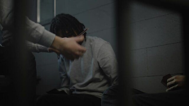 Three multiethnic teenage prisoners play cards in prison cell. Young inmates serve imprisonment term for crimes in jail. Juvenile detention center or correctional facility. View through metal bars.