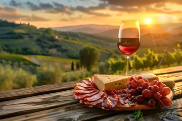 Fotobehang A serene sunset over rolling vineyard hills with a close-up of a glass of red wine and a charcuterie board. © Александр Марченко