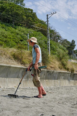 A man with a metal detector on a sandy beach in the daytime in summer.
