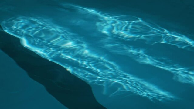 Close-up no people footage of waves of fresh cool blue water rippling in swimming pool, lane marks and sun beams dappling on bottom