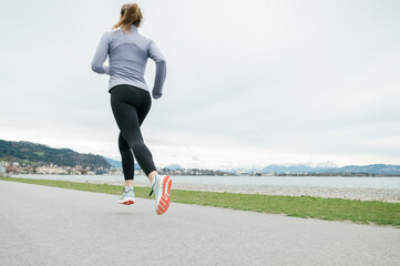 Woman jogging by lakeside with mountains in background