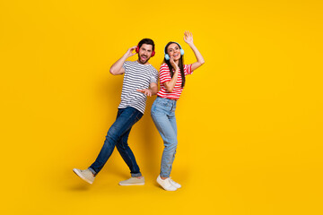 Full size portrait of two carefree partners listen music headphones good mood dancing empty space isolated on yellow color background