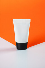 Plastic white tube for cream or lotion. Skin care or sunscreen cosmetic on orange and white background.