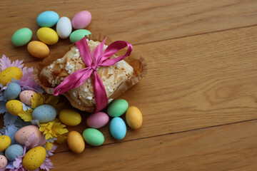 Sweet Easter cake named Colomba Pasquale (Easter dove) with pink tied bow, chocolate eggs and multicolor garland on wooden table. Italian traditional pastry 