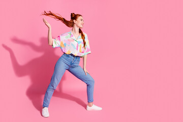 Full size photo of lovely girl with arm fluttering hair dressed colorful blouse look at logo empty space isolated on pink color background
