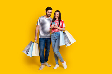 Full size photo of cheerful funny guy lovely nice girl look at smartphone holding shopping bags...