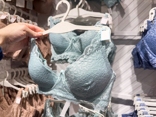 Woman chooses blue lace bra on rack in lingerie store. Female fashion underwear