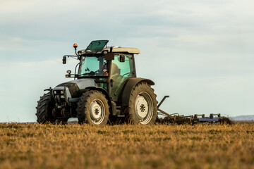 Modern tractor actively plows through farmland, creating a dynamic scene amidst an evening backdrop