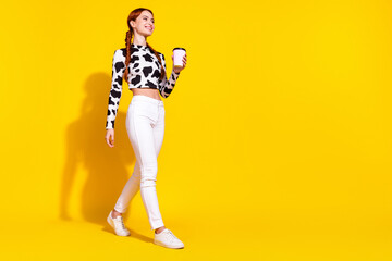 Full length photo of dreamy cute lady dressed cowskin print top enjoying milk walking empty space isolated yellow color background - obrazy, fototapety, plakaty