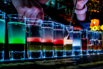 A skilled bartender pours vibrant drinks into illuminated shot glasses, creating a lively and dynamic scene at the bar