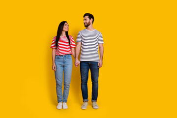 Full size photo of friendly couple girl guy dressed striped t-shirt look at each other arms together isolated on yellow color background