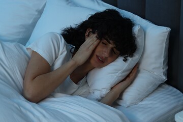 Young woman suffering from headache in bed at night