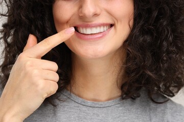 Young woman showing her teeth with whitening strip on light grey background, closeup