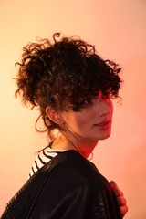 Beautiful young woman in black leather jacket posing on color background in neon lights