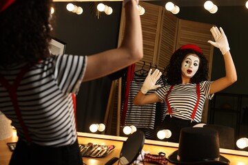 Young woman in mime costume posing near mirror indoors