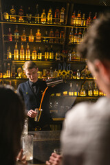 Professional barman makes delicious drink in bar with patriotic symbols. Young barkeeper prepares...