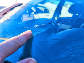 Woman Pointing Out Chip on Her Car's Windshield in Bright Daylight. A finger indicating a small...