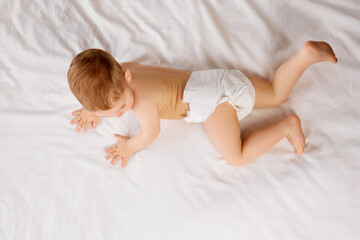 Cute little baby boy, child in diaper lying on bed, crawling, playing isolated over white studio background. Concept of childhood and family, care, parenthood, infancy and heath