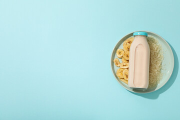 Bottle with milk on plate with rice and sliced bananas on blue background, space for text
