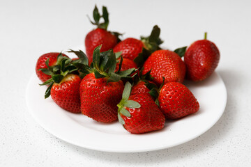 Juicy red strawberries lie on a white saucer