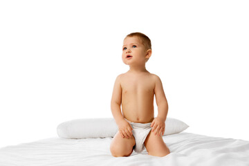 Adorable little baby boy, child sitting on bed with calm and curious face isolated over white studio background. Concept of childhood and family, care, parenthood, infancy and heath