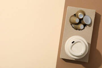 Coffee capsules and paper cup in paper stand on brown and beige background, space for text