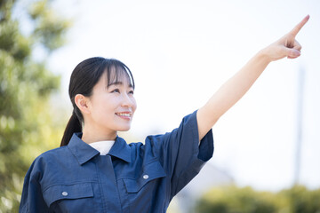 新緑の青空の屋外で作業着を着た女性　未来や目標を目指して指を差す　クローズアップ