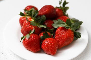 Juicy red strawberries lie on a white saucer