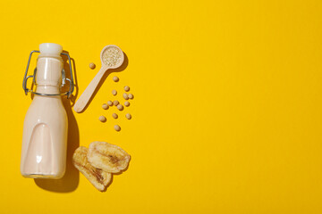 Bottle of alternative milk, soybeans and sliced bananas on yellow background, space for text