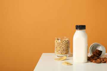 Bottle of alternative milk, nuts and soybeans on orange background, space for text