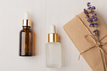 Flat lay composition with lavender cosmetic oil, face serum, eco friendly gift box with lavender bouquet on white wooden table. Herbal cosmetics and aromatherapy concept. Lavender beauty products. - obrazy, fototapety, plakaty