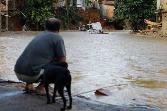 A man with his dog looks on a vehicle submerged in water during a big flood due to heavy rains in Duque de Caxias, Rio de Janeiro state, Brazil.