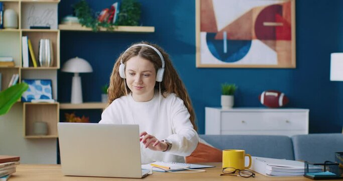 Young woman school college student wearing headphones learning, watching online webinar webcast class, looking at laptop, e-learning distance course or video calling teacher by webcam.