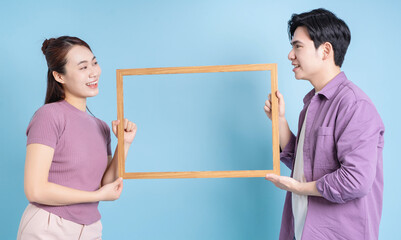 Young Asian couple holding photo frame on blue background