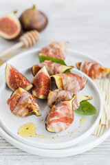 Sliced figs grilled and wrapped in crispy bacon served with basil and  honey on a plate, sweet and savory party appetizer