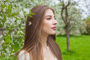 Young brunette woman portrait. Beautiful female model with long hair and make-up in spring garden outdoor