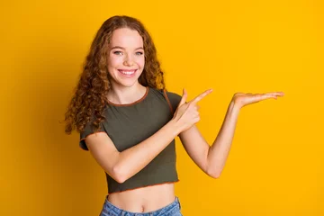 Fototapeten Photo of adorable cute girl wear stylish clothes arms demonstrate empty space logo brand isolated on yellow color background © deagreez