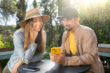 Happy man and woman looking at a cell phone together outdoors during sunny day. High quality photo