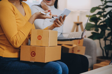 Asian SME business women use laptop computer checking customer order online shipping boxes at home....