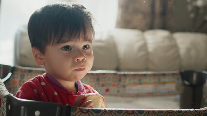 Two-year-old Asian kid eats an apple, stands in his crib