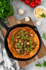 Savory Dutch baby pancake with cheese, fried mushrooms and arugula in cast iron pan on a concrete background. Vegetarian breakfast.