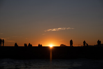Fototapeta na wymiar Seaside at sunset with small groups of people in silhouette 