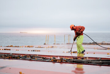Seaman Seafarer In Safety Clothes Working On Deck Hatch Holding The Water Blasting Jet Machine....