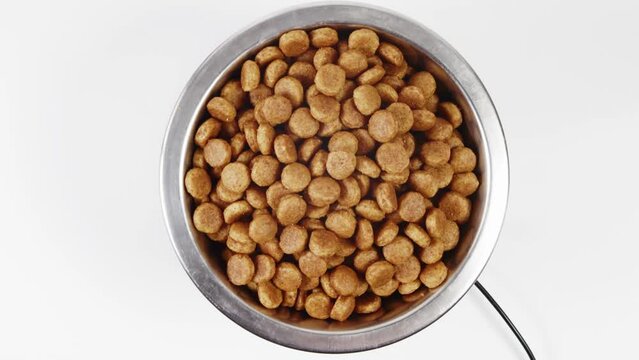 Dry food in a bowl on a white background rotates slowly, top view. Bowl with dry pet food on white background. Dried dog food background. 