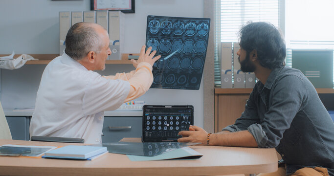 Portrait of Indian Male Patient Having a Doctor Appointment in Hospital. Professional Neurologist Using MRI Scan Images and Digital Tablet to Give Diagnosis and Suggestions to his Patient